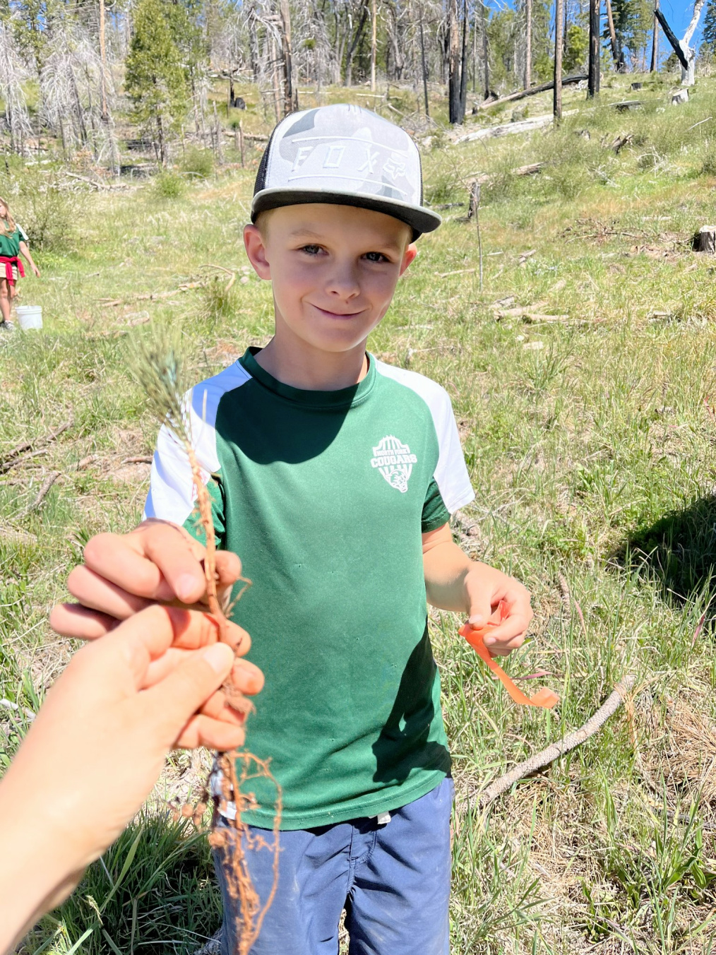 Smiling student volunteer taking a tree seedling from another person's hand